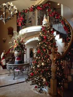 a decorated christmas tree sitting in the middle of a living room next to a staircase