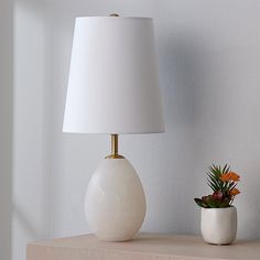 a white lamp sitting on top of a wooden table next to a potted plant