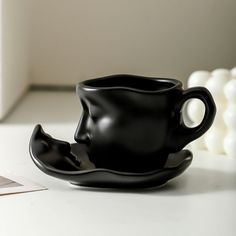 a black coffee cup sitting on top of a white table