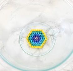 a beaded object in a glass bowl on a marble countertop, with water droplets around it