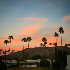 palm trees are silhouetted against the sunset in front of a house and mountain range