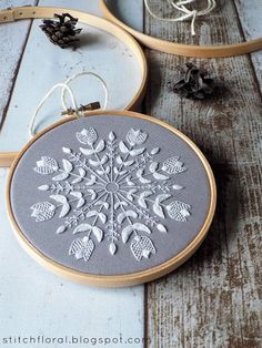 two embroidery hoops sitting next to each other on a wooden floor with pine cones