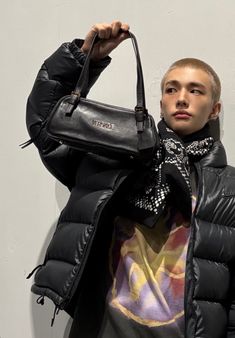 a young man holding onto a black handbag in front of his face and looking at the camera