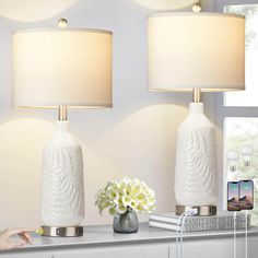 two white lamps sitting on top of a table next to a vase with flowers in it