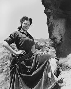 an old photo of a woman in a dress standing next to a rock formation with her hands on her hips