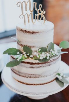 a three tiered cake with greenery and the word mr and mrs on top