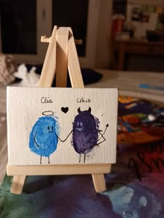 an easel with a painting on it that has two little blue monsters painted on it