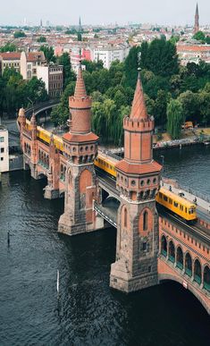 a yellow train traveling over a bridge in the middle of a river next to tall buildings