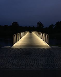 a bridge lit up at night over a body of water with trees in the background