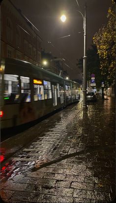 a train is traveling down the tracks in the rain at night with its lights on