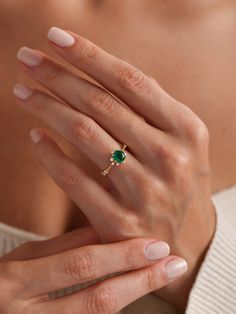 a woman's hand wearing a ring with an emerald stone in the middle and a diamond on top