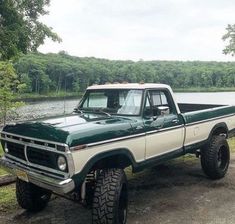 a green and white pickup truck parked next to a lake with trees in the background