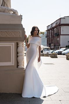 a woman in a white wedding dress leaning against a wall with her hand on her hip