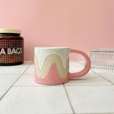 a pink and white mug sitting on top of a tiled floor next to a jar