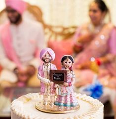 a cake with two figurines on top of it and people in the background