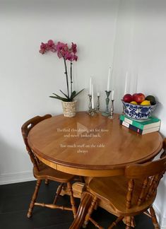 a wooden table topped with two chairs next to a vase filled with flowers and fruit