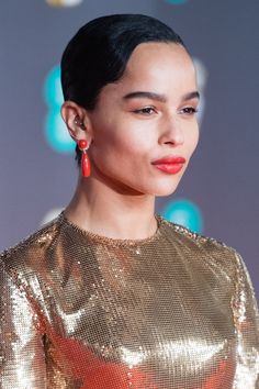 a woman with black hair wearing red earrings and a gold top is looking off to the side