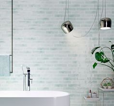 a white bath tub sitting next to a green plant in a room with brick walls