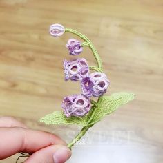 a hand holding a crocheted flower on top of a wooden table