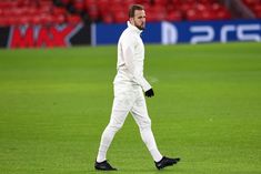 a man in white is walking on the field with his foot up and wearing black shoes