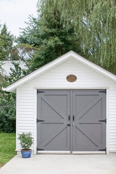 a white shed with two doors and a potted plant