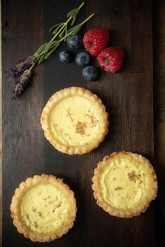 three pies sitting on top of a wooden table next to berries and raspberries