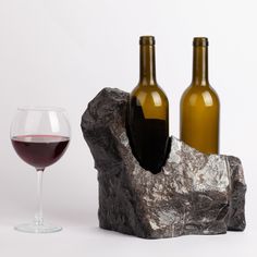 two wine bottles and a glass on a rock