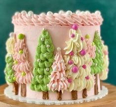 a cake decorated with pink, green and white frosting trees on top of a wooden table