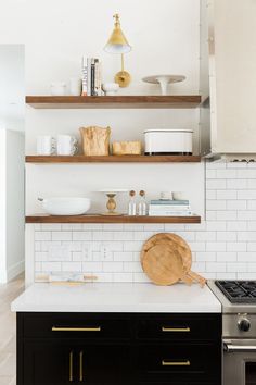 a kitchen with black cabinets and white subway backsplash, gold accents on the shelves