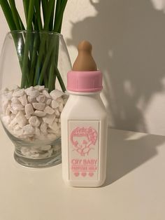 a baby bottle next to a vase filled with flowers and marshmallows on a table