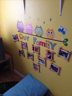 a yellow wall with pictures hanging on it and an owl family magnet board attached to the wall