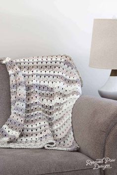 a crocheted blanket sitting on top of a gray couch next to a lamp