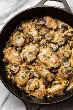 a skillet with chicken, mushrooms and gravy in it on a marble surface