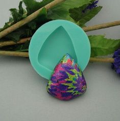 a blue plastic spoon sitting next to purple flowers and green leafy stems on a white surface