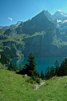 there is a mountain range in the background with trees and grass on it, as well as a body of water