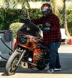 a man on a motorcycle with flames painted on the front and back fenders, standing next to a gas pump