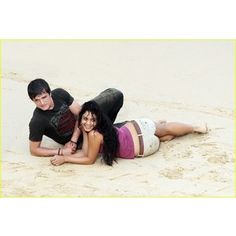 two people are laying on the sand in their bathing suits and posing for a photo