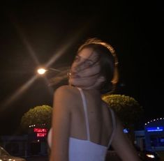 a woman in a white dress standing on the street at night with her eyes closed