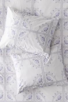 two pillows on top of a bed with white sheets and blue patterned pillowcases