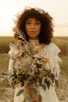 a woman in a white dress holding a bouquet of wildflowers and grasses with her face close to the camera