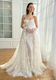 a woman in a white wedding dress standing on a wooden floor with her hands behind her back