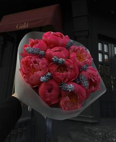 a person holding a bouquet of pink flowers in front of a black building at night