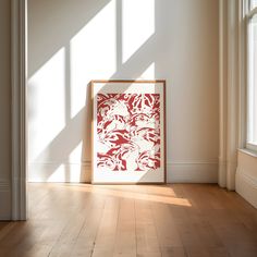 a red and white painting sitting on top of a wooden floor next to a window