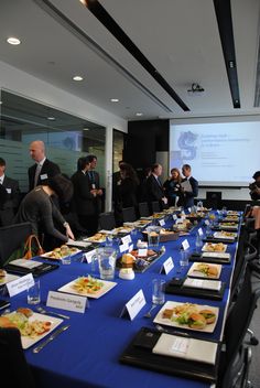 a group of people standing around a long table with food on it and drinks in front of them