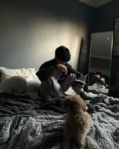 a person sitting on a bed with a dog looking at their reflection in the mirror