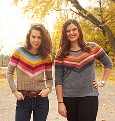 two young women standing next to each other in front of trees with leaves on the ground