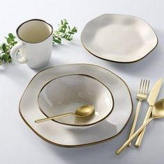 a table setting with white dishes and gold rimmed utensils, including a coffee cup