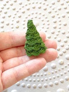 a small green crocheted christmas tree in someone's hand on a white surface