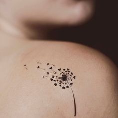 the back of a woman's shoulder with a dandelion tattoo