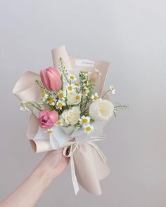 a hand holding a bouquet of flowers with white and pink blooms on it's side